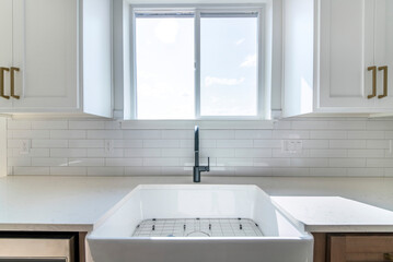 White porcelain sink with black single faucet in a kitchen against the window