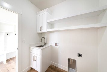 Empty laundry room with single vanity sink, wall cabinets and shelves