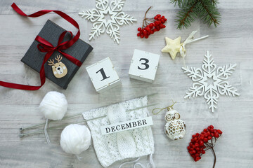Calendar for December 13: New Year's decor, a gift tied with a red ribbon, knitting from white yarn, spruce branches and viburnum berries, the number 13, the name of the month in English.