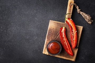 Spicy sauce. Ketchup with pepper. Hot red pepper on a wooden board. Chili pepper on a black background. Place for text in a food photo