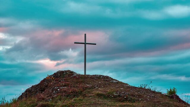 Iron Christian cross on a rocky hill. Colorful clouds in motion at sunset.