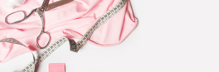 Tailoring concept. Accessories for sewing and needlework. pink fabric, scissors and measuring tape....