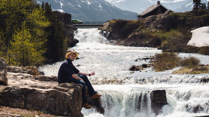 Obraz premium man sitting on rock by waterfall