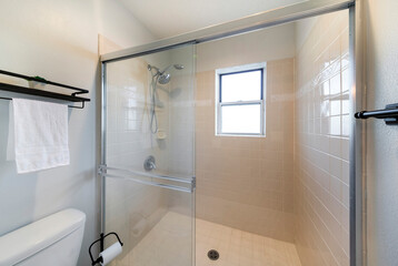Shower stall inside a bathroom with beige square tiles and sliding glass door