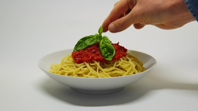 Il basilico viene messo su un piatto di spaghetti al pomodoro