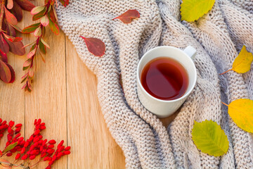 Autumn flatlay on a wooden background with a cup of tea, knitted sweater, barberry branches and fallen autumn leaves. Home coziness concept
