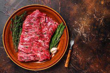 Raw beef skirt meat steak on a rustic plate with herbs. Dark background. Top view. Copy space