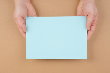 Woman holds a blank sheet of paper, brown colored background, empty copy space for text, minimalism