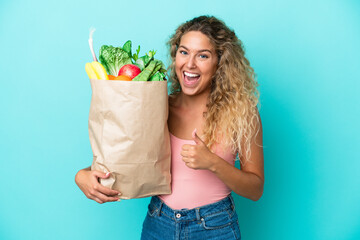 Girl with curly hair holding a grocery shopping bag isolated on green background giving a thumbs up gesture