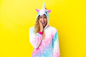 Girl with curly hair wearing a unicorn pajama isolated on yellow background with surprise and shocked facial expression