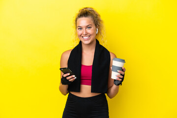 Sport woman with towel isolated on yellow background holding coffee to take away and a mobile