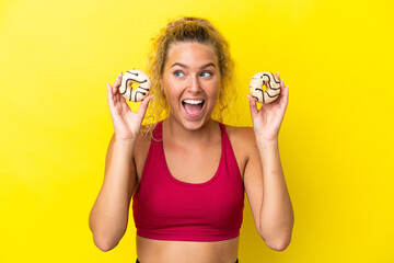 Girl with curly hair isolated on yellow background holding donuts and surprised