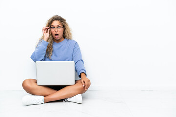 Girl with curly hair with a laptop sitting on the floor with glasses and surprised