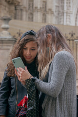 Portrait of friends looking at their cell phones in the middle of the street in Seville, looking for a tourist destination to visit.