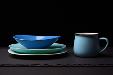 A stack of plates of blue and birch color, a blue glass in the form of a pot on a dark stand of stone.