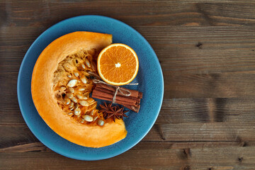 Fresh organic pumpkin slice, oranges and spices on a blue plate