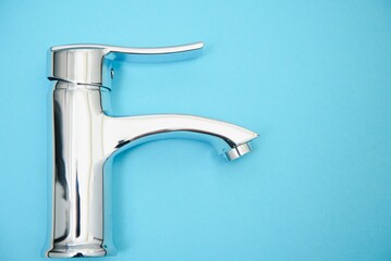 Single handle water tap on light blue background. New chrome or steel mixer tap .