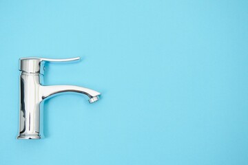 Single handle water tap on light blue background. New chrome or steel mixer tap .