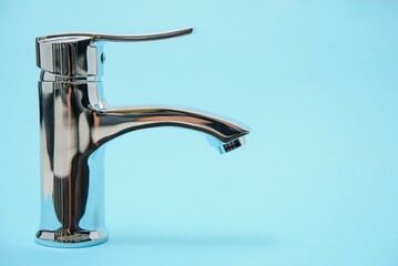 Single handle water tap on light blue background. New chrome or steel mixer tap .