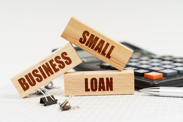 On the table is a pen, a calculator and small wooden blocks with the inscription - SMALL BUSINESS LOAN