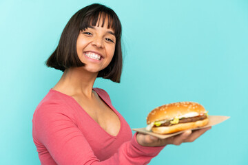 Young brunette woman holding a burger over isolated background