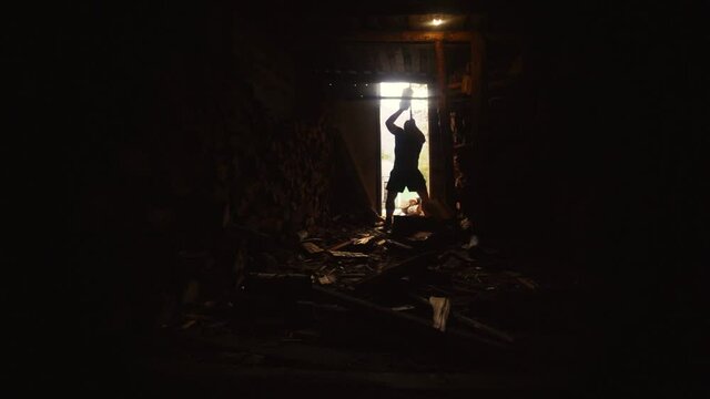 Silhouette of a man chopping wood in a barn