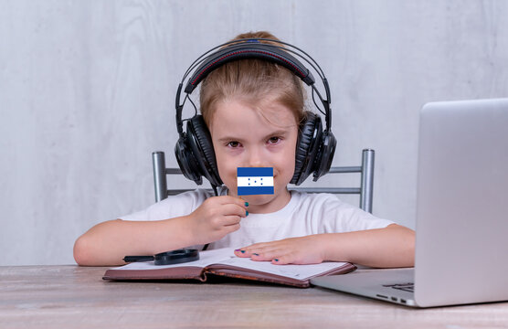 School Female Child With Honduras Flag. Child In Headphones, With A Book And Laptop Has Lesson Online