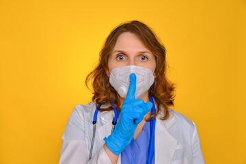 Woman nurse in a medical mask put a finger to her lips with a gesture about not spreading rumors...