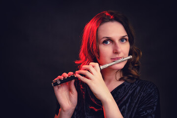 Portrait of a woman musician with a piccolo flute on a studio black background. Flutist with a small flute in her hands - obrazy, fototapety, plakaty