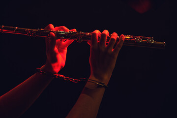 Hands of a woman musician with a flute in handcuffed hands on a black studio background. Problems of musical playing at concerts, the concept of non-freedom and arrests