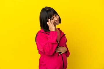 Young pregnant woman over isolated yellow background with headache
