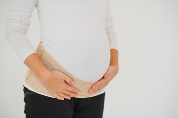 Close up of pregnant woman putting on a bandage at gray background with copy space. Orthopedic abdominal support belt concept.
