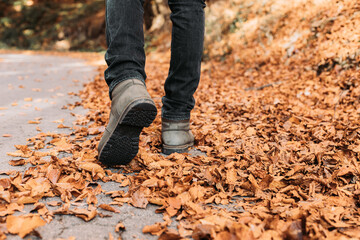 Male with winter boots walking through fallen autumn leaves