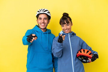 Young cyclist couple isolated on yellow background points finger at you with a confident expression
