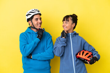 Young cyclist couple isolated on yellow background looking looking at each other