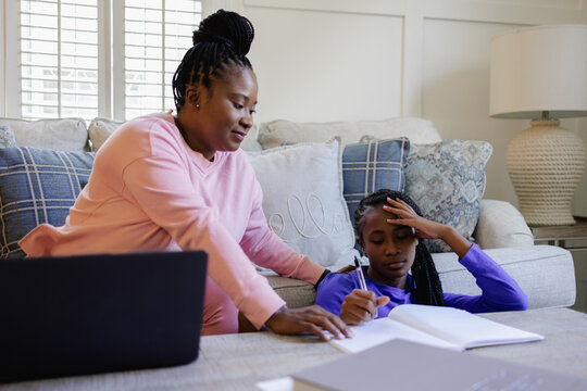 African American Mother assisting teenage daughter doing homework at table in living room