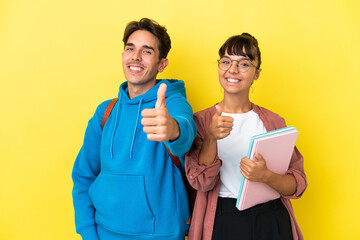 Young student couple isolated on yellow background giving a thumbs up gesture because something...