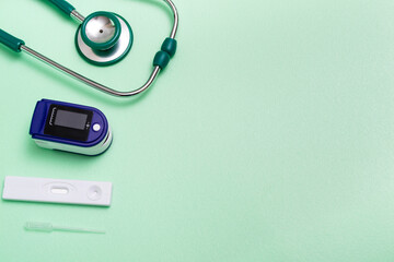 Medical concept. Top view flat lay close up of stethoscope, pulse oximeter and express test for coronavirus on green background. copy space.