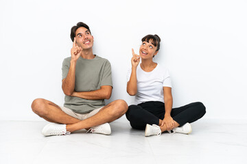 Fototapeta na wymiar Young mixed race couple sitting on the floor isolated on white background pointing a great idea and looking up