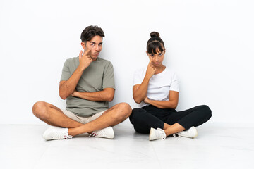 Young mixed race couple sitting on the floor isolated on white background looking to the front