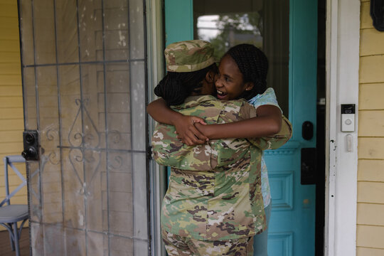 Military woman in camouflage uniform hugging daughter in front of house
