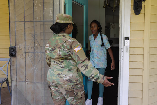 Happy teenage girl greeting military mother in camouflage uniform in doorway