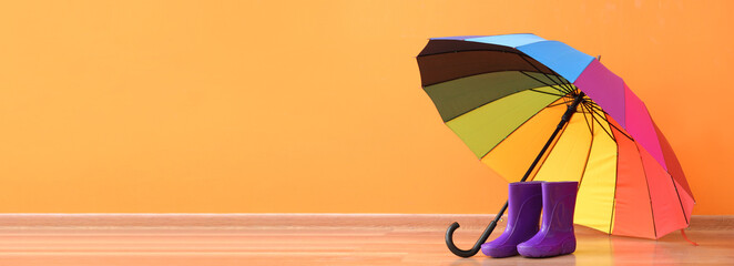Rubber boots with umbrella on color background with space for text