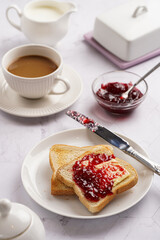 sweet breakfast - toast bread with butter and cherry jam on a white plate, cup of cappuccino