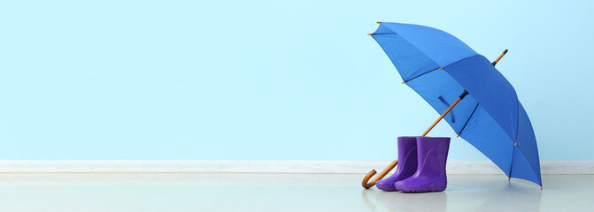 Pair of rubber rain boots and umbrella on color background with space for text