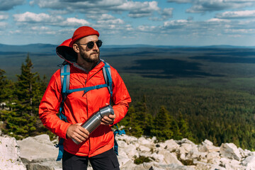 A bearded traveler with a backpack on the top of a mountain. Portrait of a traveler in a red cap...