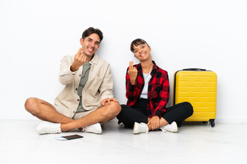 Fototapeta premium Young mixed race travelers couple sitting on the floor isolated on white background inviting to come with hand. Happy that you came