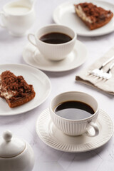 sweet breakfast - two white porcelain cups with coffee drink on a white saucer, piece of brown cake