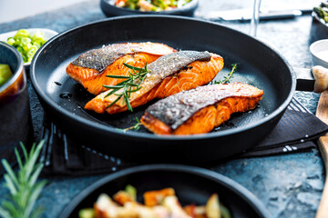 Gebratener Lachs serviert in einer Pfanne mit Beilagen Salat.