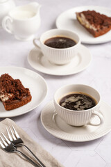 sweet breakfast - two white porcelain cups with coffee drink on a white saucer, piece of brown cake